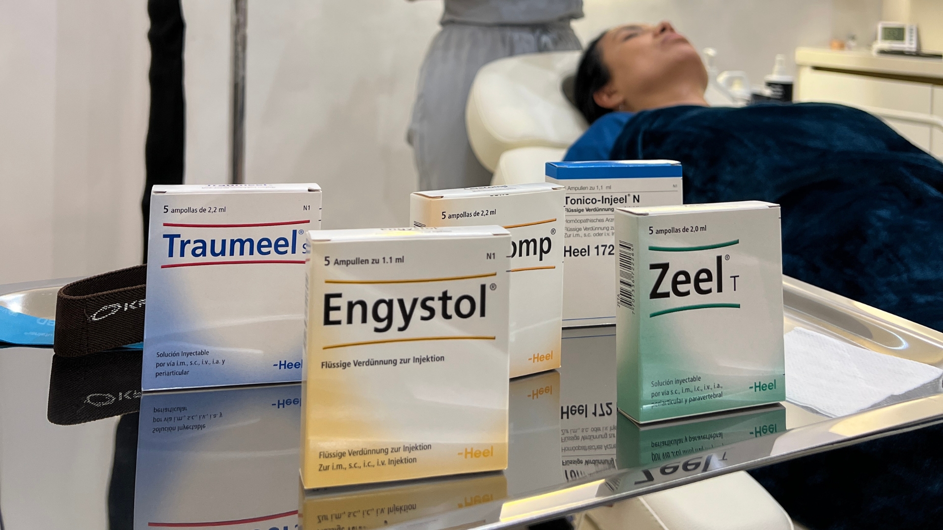 Medicamentos homeopáticos como Traumeel, Engystol y Zeel sobre una mesa en consultorio, con paciente recostada recibiendo sueroterapia en Bogotá