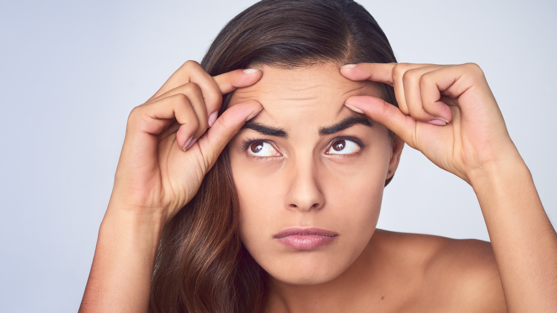 1 (1) Mujer joven tocándose la frente y frunciendo el ceño, mostrando líneas de expresión